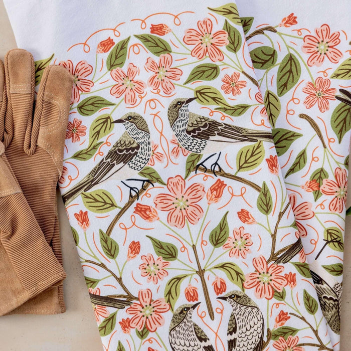 Floral and bird patterned fabric with brown gloves on a white background