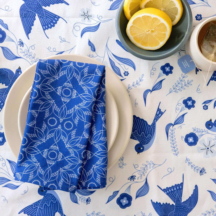 Table setting with blue and white patterned tablecloth, plate, and napkin.
