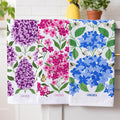 Three floral towels with purple, pink, and blue flowers displayed on a rack.
