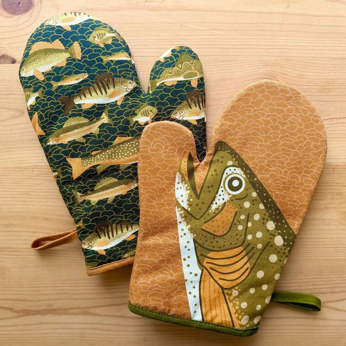 Set of oven mitts and pot holder with fish design on a wooden surface