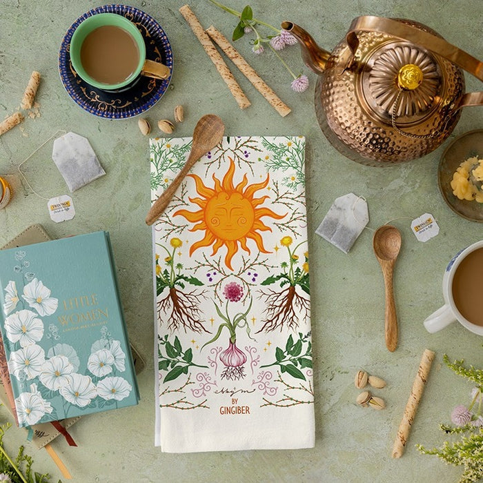 Tea towel with sun and plant design on a table with tea accessories