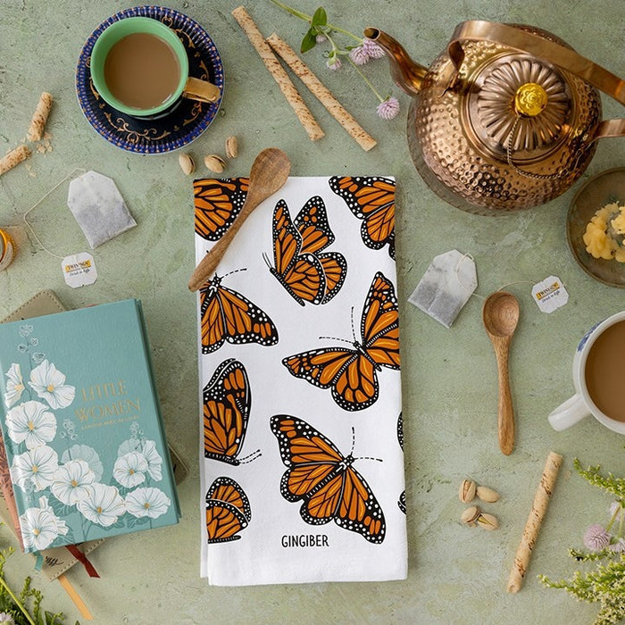 Butterfly-themed towel on a table with tea-making items and a book.