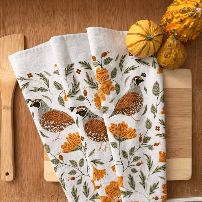 Set of three decorative towels with floral and bird patterns on a wooden surface with pumpkins.