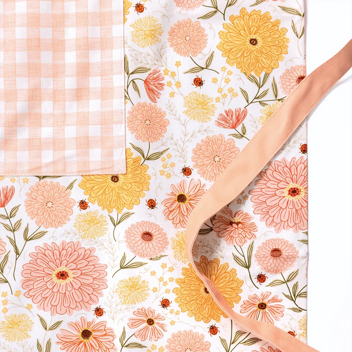 Zinnia Apron product image showcasing floral print and gingiber design with soft peach piping and tied waist, 100% cotton canvas